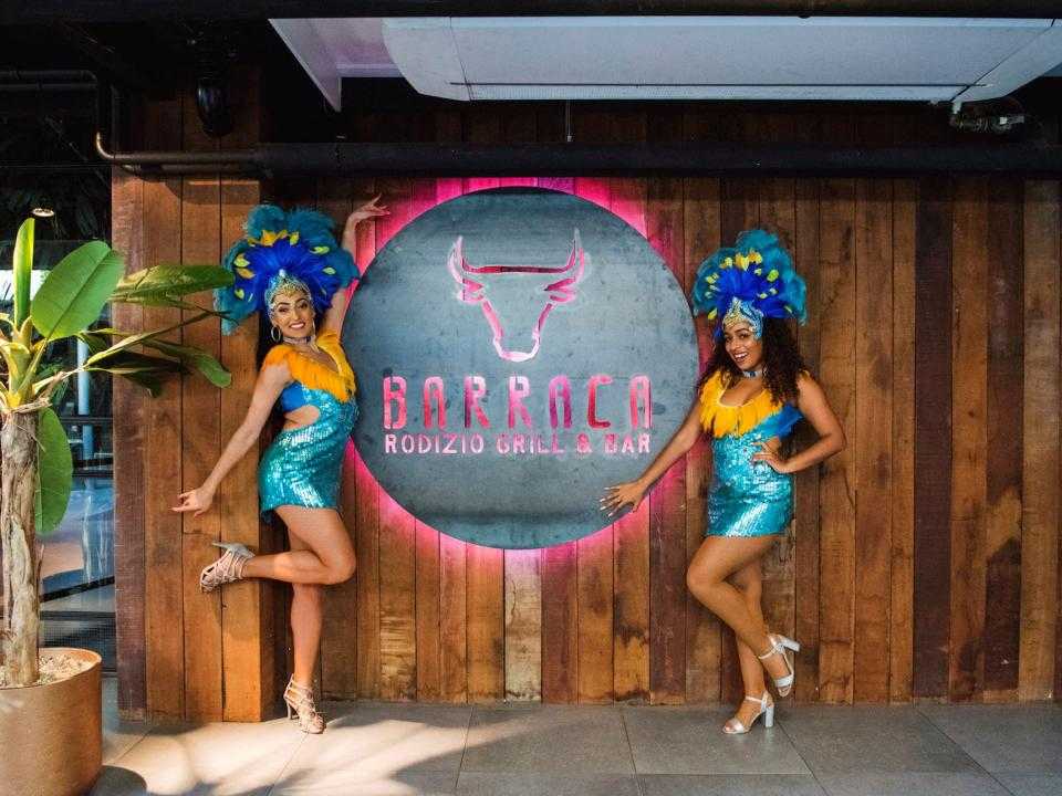 2 dames in Braziliaanse kleding met hoofdtooi bij logo Barraca in restaurant
