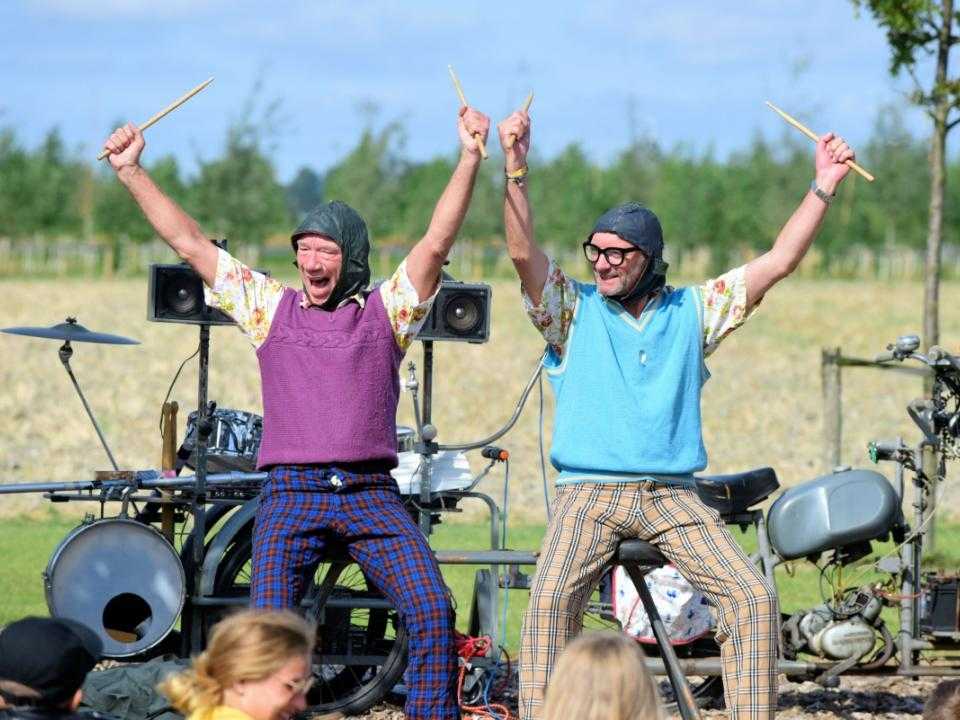 Optreden van 2 mannen met de armen in de lucht en een drumstel op de achtergrond