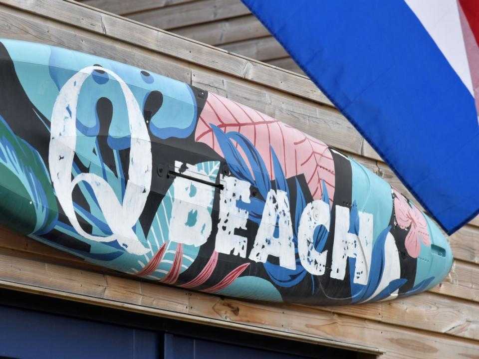 Surfplank aan muur met tekst qbeach met stukje van de nederlandse vlag