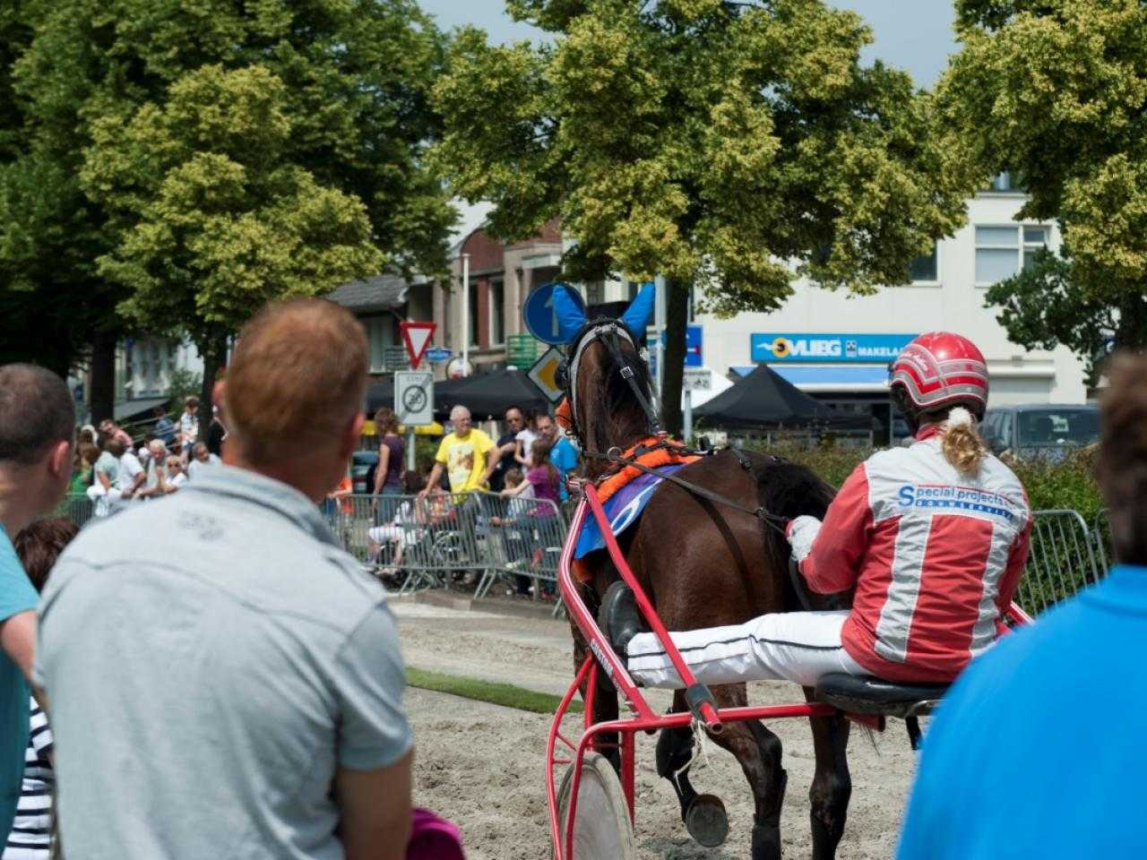 Publiek bij Kortebaandraverij en op achtergrond jockey met paard