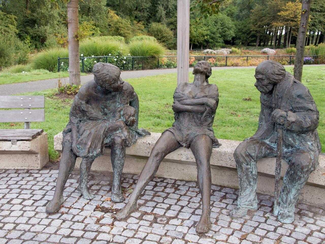 Sculpture Karel Gomes in Haarlemmermeerse Bos. Recreationists: a woman with a baby on her lap has a chat with an old man. Between them, on the bench at the edge of the lake, a young girl is sunbathing