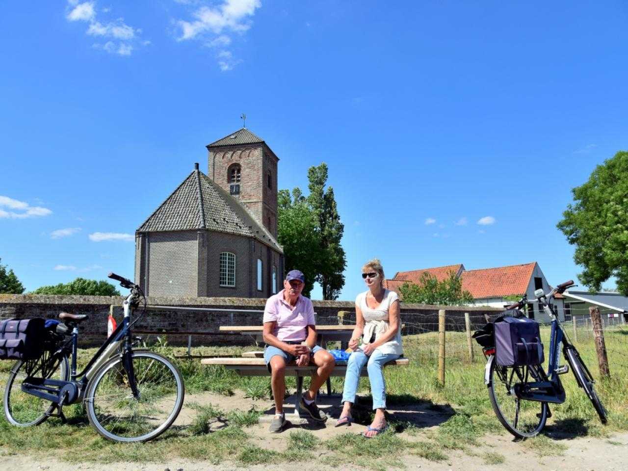 Man and woman on a bench with bicycles next to them with a stubby tower in the background