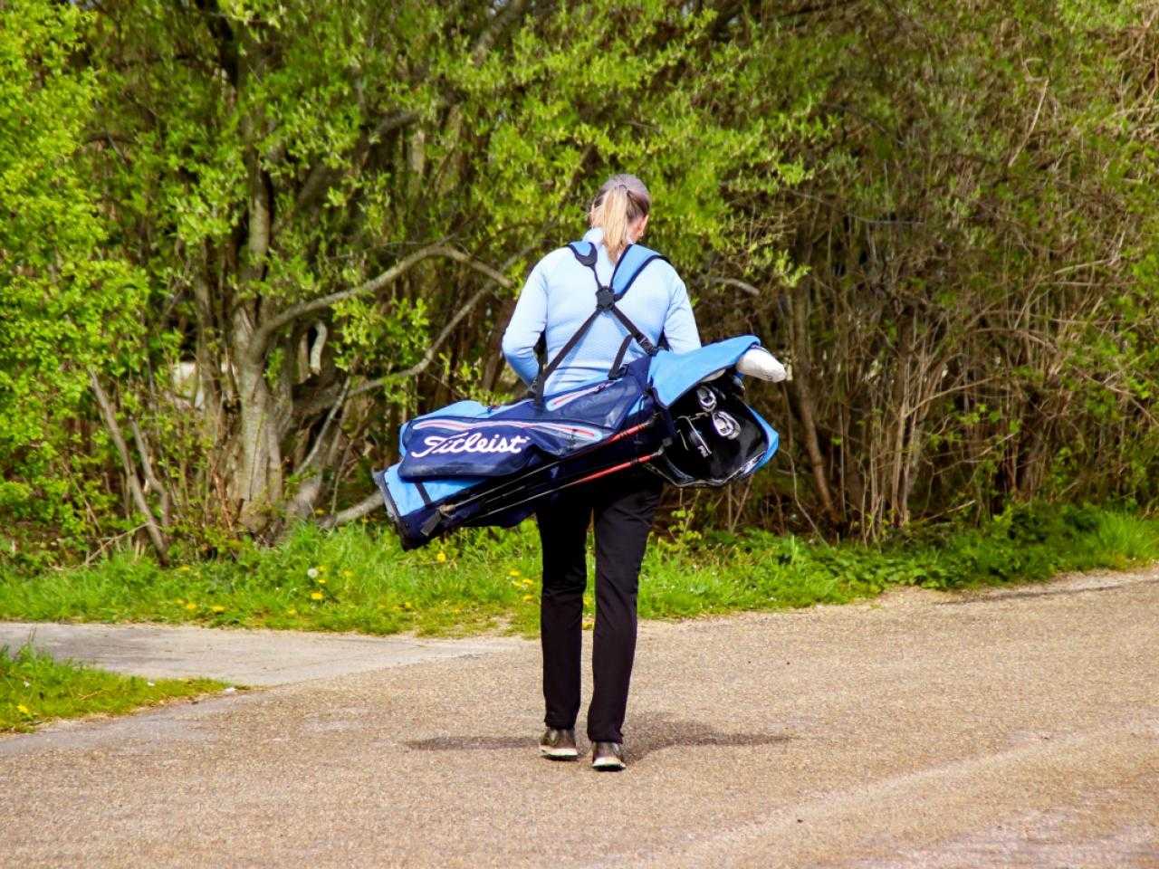 Golfer met tas over schouder lopend op pad