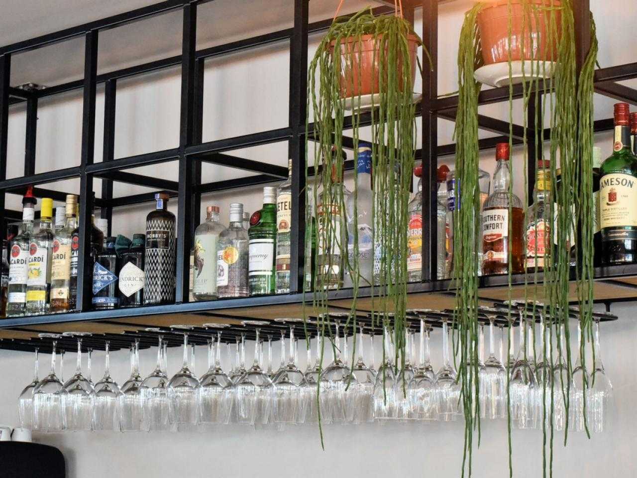 Wijnglazen hangend aan bar met flessen drank erboven bij restaurant Nobel