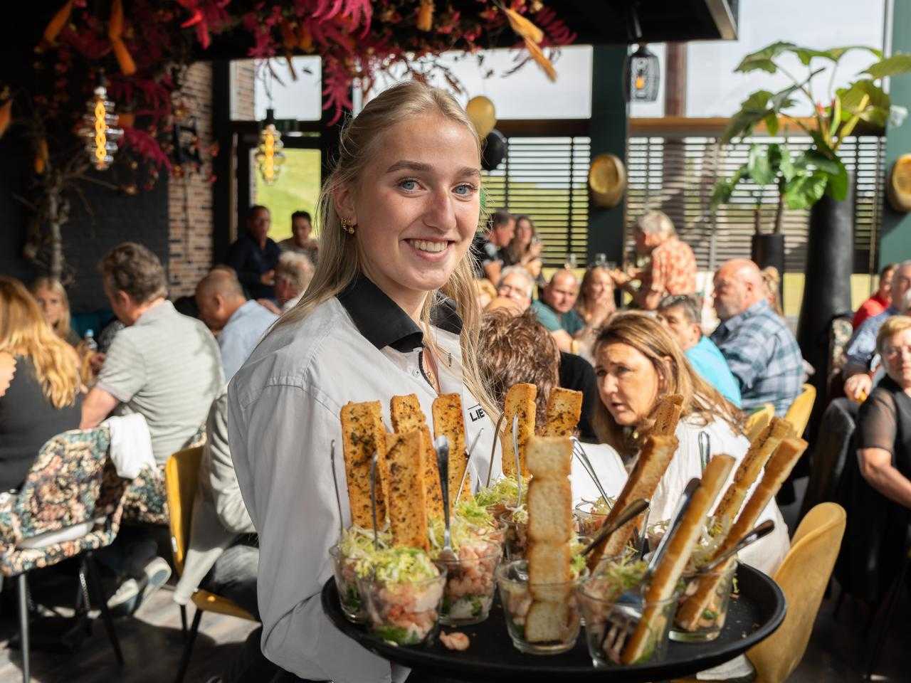 Bediening met eten in hand en etende gasten op achtergrond